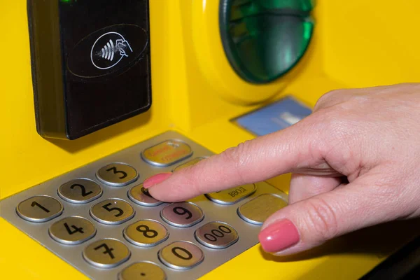 A woman's hand dials the PIN code on the bank's ATM. A young woman enters a PIN code on the ATM keyboard