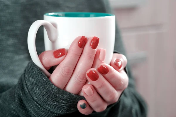 Hot coffee in a Cup. The girl holds a Cup of coffee in her hands. Warms your hands. Sitting in a chair at home in quarantine.