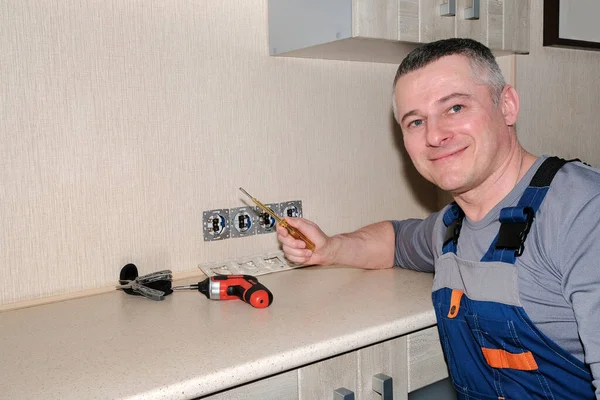 An electrician installs electrical outlets in the kitchen. Tools in hand. Modern design. — Stock Photo, Image