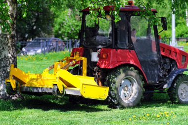 Küçük bir traktör çimleri biçer. Evlerin arasındaki alanın peyzajı. Şehir bahçesi.