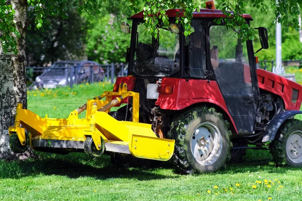 Egy kis traktor nyírja a füvet. Parkosítás a terület között a házak. Városi kert. — Stock Fotó