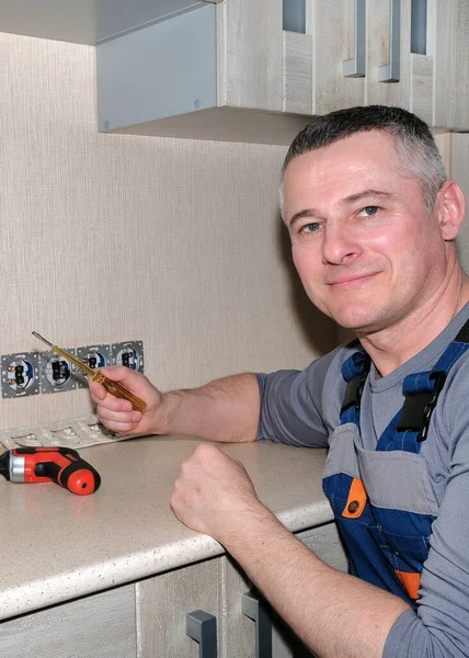 An electrician installs electrical outlets in the kitchen. Tools in hand. Modern design. — Stock Photo, Image