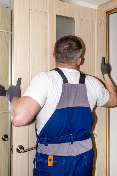 A master carpenter in a blue jumpsuit installs a wooden interior door. — Stock Photo, Image