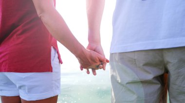 Kumsalda gün batımında el ele tutuşan çift. Aşık romantik genç çift.