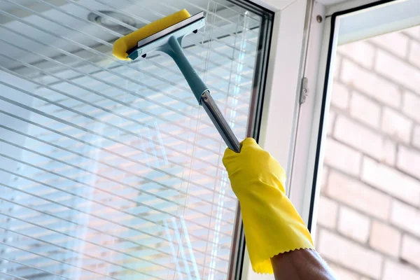 Ein Mitarbeiter einer Reinigungsfirma in Handschuhen wäscht das Fenster mit einem Pinsel mit einem Fensterschaber. — Stockfoto