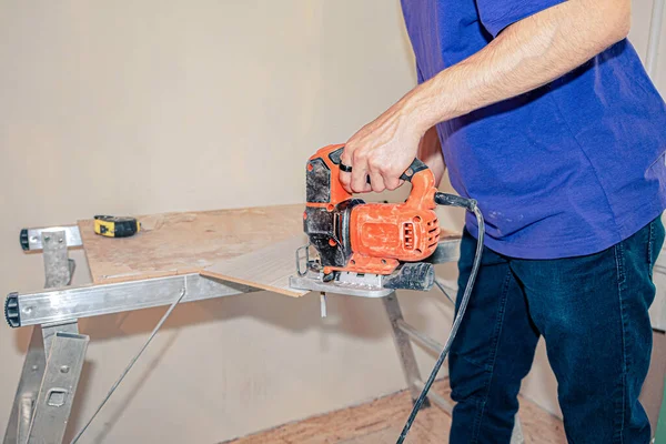 Der Meister schneidet das Laminat auf der Werkbank mit einer Stichsäge — Stockfoto