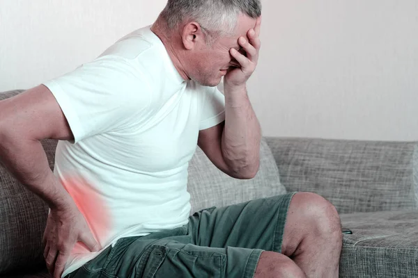 Un hombre se aferra a la parte inferior de la espalda, reumatismo, espasmos musculares, espalda y dolor de espalda. —  Fotos de Stock