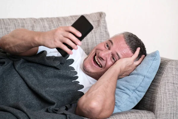 Ein schönes Porträt eines Mannes, der lacht, während er auf sein Smartphone blickt. Mobilfunk. Online-Kommunikation. — Stockfoto