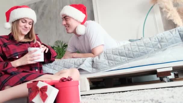 Karácsonyi otthon gratulálok. Boldog mosolygós pár ajándék doboz visel Mikulás kalap — Stock videók