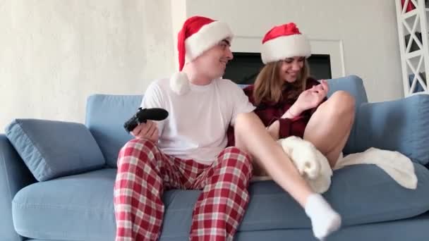 Video games and leisure concept. Man and a woman playing console holding gamepads sitting at home on the couch wearing pajamas and Christmas hats. Woman loses, gets upset and leaves. Slow motion — Stock Video