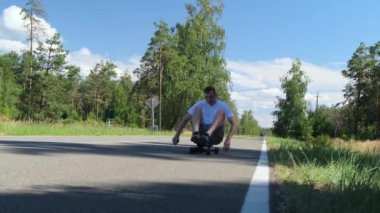 Genç bir adam kaykaya biniyor ve elleri asfaltta ağaca doğru itiyor, ağır çekimde.