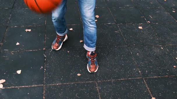 Dribbling with a basketball. A man in jeans and sneakers stuffs an orange leather ball wilson evolution on a black tile. Kiev, Ukraine, October 22, 2020 — Stock Video