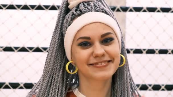 Портрет щасливої молодої жінки з дредлоками або канекалонськими косами, які дивляться на камеру і посміхаються в білому поясі і жовтих сережках — стокове відео