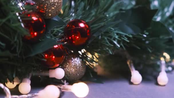 Nieuwjaar of kerst achtergrond. Close-up van de kunstmatige dennenboom versierd met rode en gouden kerstballen en knipperende slinger gloeilampen — Stockvideo