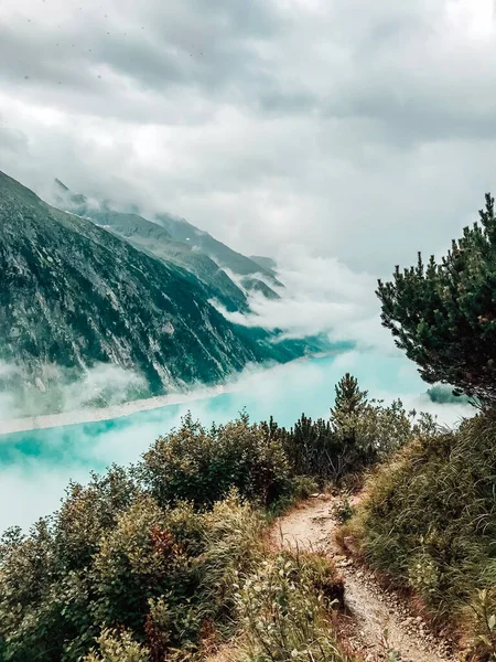 전나무들 사이로 구름과 안개로 덮여 있는 맑은 청록색 산 슐레 가이스 호수를 바라본다. Zillertal Alves, Mayrhofen, Austria. 수직 촬영 — 스톡 사진