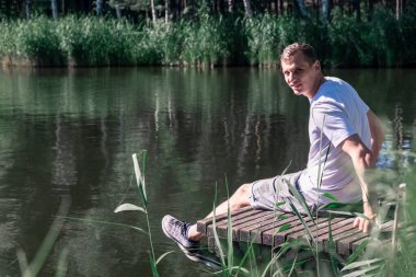 Güneşli bir yaz gününün tadını çıkaran mutlu, rahat bir adam. Etrafı yeşilliklerle çevrili ve kameraya bakan ağaçlarla çevrili. Akıl sağlığı, yeniden başlat