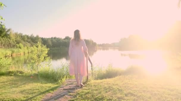 Молодая блондинка в очках прогуливаясь по озеру на закате в летний вечер, 4k — стоковое видео