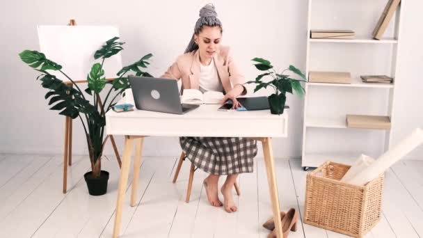 Aantrekkelijke jonge blote voeten blanke vrouw in een roze jasje zit in een kantoor aan een tafel met een open laptop. Ze neemt de telefoon op en legt haar voeten op de tafel. Langzame beweging, 4k — Stockvideo