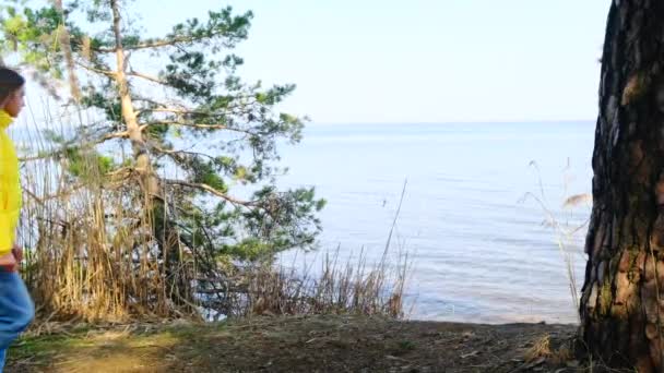 Turistka s batohem je zapojena do pěší turistiky v lese na břehu obrovského jezera nebo řeky. Blíží se k okraji rybníka a rozprostírá se s nádherným výhledem na slunný jarní den. 4k — Stock video