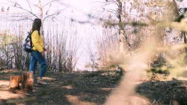 Turizm, iyileşme, akıl sağlığı. Büyük bir sırt çantası ve sarı ceketli genç bir kadın nehre doğru yürür, durur, ellerini kaldırır ve güzel manzaranın ve temiz havanın tadını çıkarır. 4k