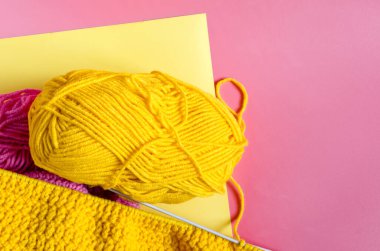 Renkli bir arka planda örgü iğneleriyle örülmüş parlak sarı iplik yumağı. Kendi kendini izole eden örgü konseptinin arka planında.