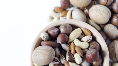 Seramik tabaklarda çeşitli fındıklar ve fındıklar beyaz arka planda çeşitli fındıklara saçılmış.