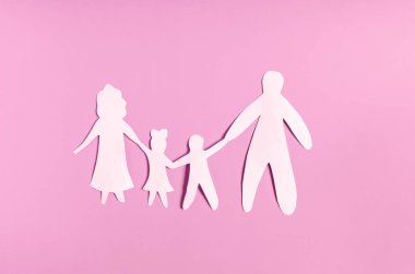 Pembe arka plandaki insanların beyaz kağıt figürleri. Aile ilişkileri kavramı. Yetişkinlerin ve çocukların karton figürleri.