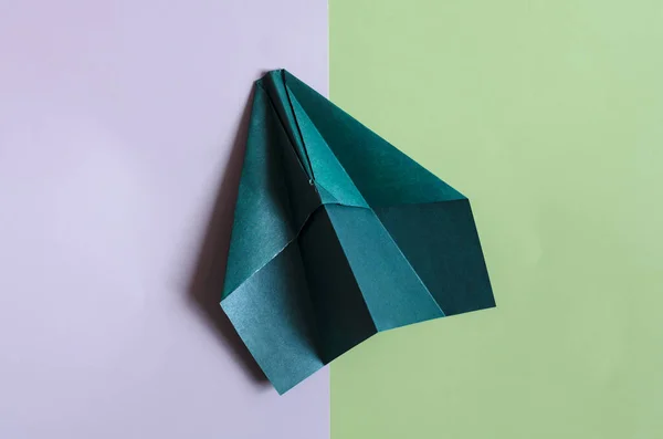 A green concept paper airplane on a two-tone purple-green background. Origami bright green paper airplane