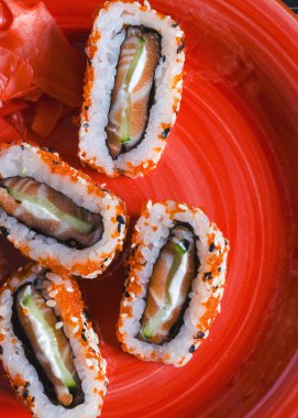 Kırmızı tabakta susam ve zencefille süslenmiş balık, salatalık ve peynirli rulo. Kırmızı rulo yakın - dikey yönelimli