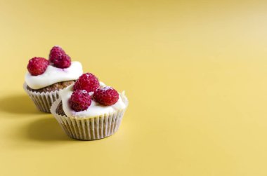 Sarı arka planda beyaz kremalı ve ahududulu kekler. Renkli arka planda ev yapımı tatlı kekler metin için bir yerdir..