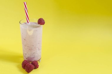 Şeffaf bardakta milkshake, ahududu ve parlak sarı arka planda kırmızı bir tüp. Renkli bir arka planda metin için dondurma, süt ve dut kokteyli
