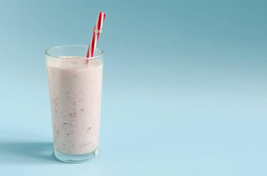 Açık mavi arka planda kırmızı bir tüple şeffaf bir bardakta milkshake. Renkli bir arka planda metin için dondurma, süt ve dut kokteyli