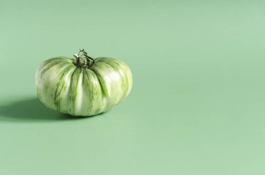 Kopi uzayının açık yeşil arka planında yeşil bir domates. Sebze yeşili domates yakın.