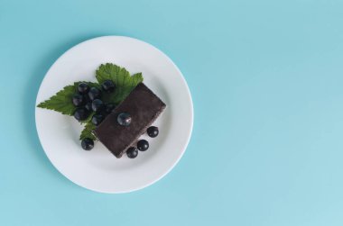 Kahverengi kremalı kek, siyah frenk üzümü yaprakları ve beyaz tabakta böğürtlen. Siyah böğürtlen ve kek renkli bir arkaplan kopyalama alanı