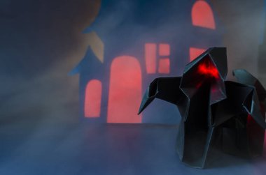 Karanlık bir evin arka planında sislerin içinde kırmızı parıldayan iki karanlık hayaletin figürleri. Cadılar bayramı için siyah kağıt hayaletler.