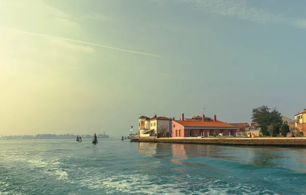 The bright rays of the rising sun illuminate residential buildings located on the very coast of the island. Canals are streets for movement.