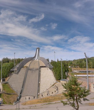 Oslo, Norveç - Temmuz 2018. Yazın Holmenkollen kayak atlayışının panoramik görüntüsü. Kayak atlayışı, alt manzara. Parlak mavi gökyüzü ve yeşil çimen Olimpiyat salonunun güzelliğini vurguluyor.