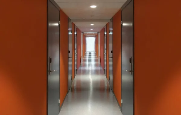 Long empty corridor with orange doors. Light space at the end of the corridor. The concept of finding a way out and hoping for the best. Synchronous perspective