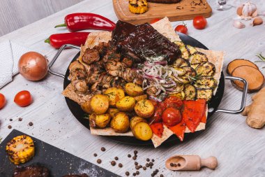 Süslü ve patatesli yuvarlak tabakta çeşitli et ve kebaplar.