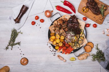 Süslü ve patatesli yuvarlak tabakta çeşitli et ve kebaplar.