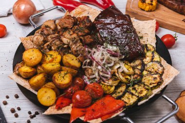 Süslü ve patatesli yuvarlak tabakta çeşitli et ve kebaplar.