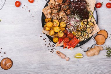 Süslü ve patatesli yuvarlak tabakta çeşitli et ve kebaplar.