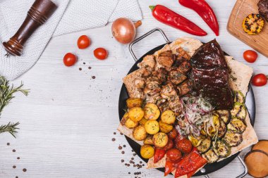 Süslü ve patatesli yuvarlak tabakta çeşitli et ve kebaplar.