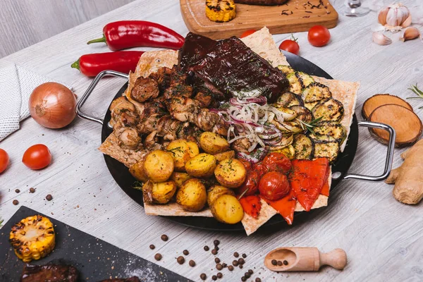 Süslü ve patatesli yuvarlak tabakta çeşitli et ve kebaplar.