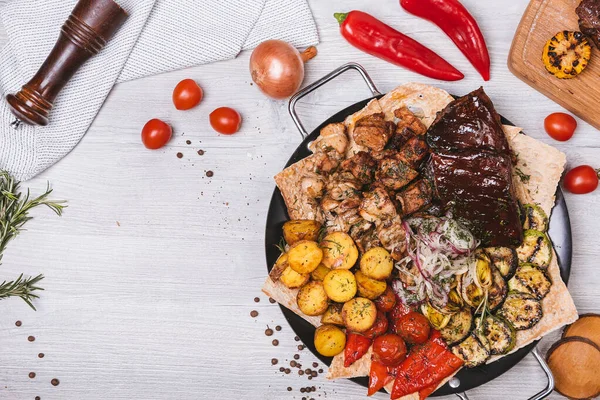 Süslü ve patatesli yuvarlak tabakta çeşitli et ve kebaplar.