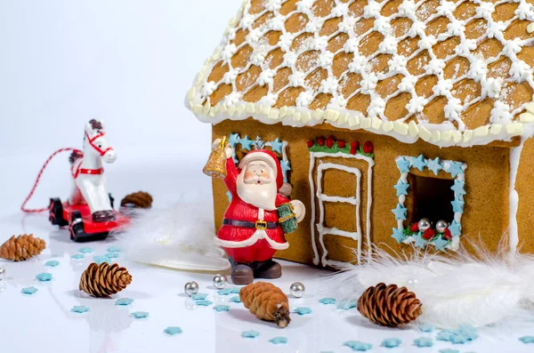 Gingerbread house decorated with glaze on a light background. Holiday decorations. Figurines of a Christmas tree, a horse and Santa Claus. Festive mood