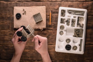 Bir çocuk kahverengi ahşap tezgahta oyuncak araba inşa setini monte ediyor..