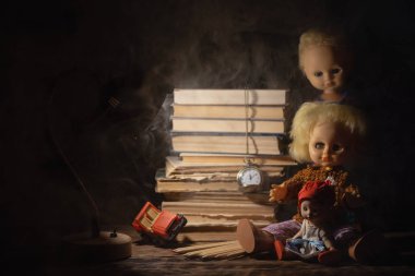 Eski oyuncak bebek ve kitap yığını karanlık arka planda masanın üstünde..