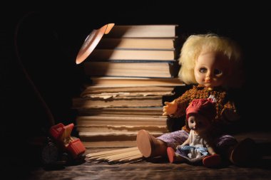 Eski oyuncak bebek ve kitap yığını karanlık arka planda masanın üstünde..