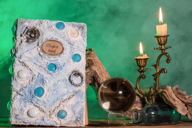 Beyaz sihirli kitap, kristal küre ve yanan mum yeşil duman arka planda masada.